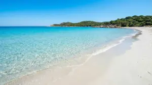 Spiaggia di sabbia bianca con mare cristallino e colline verdi sullo sfondo
